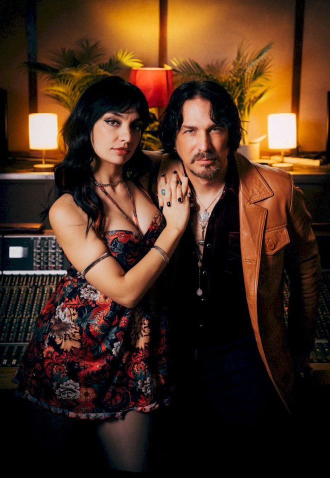 WHEN RIVERS MEET Tide Is Turning - woman in floral dress and man in leather jacket standing together in lamp-lit room