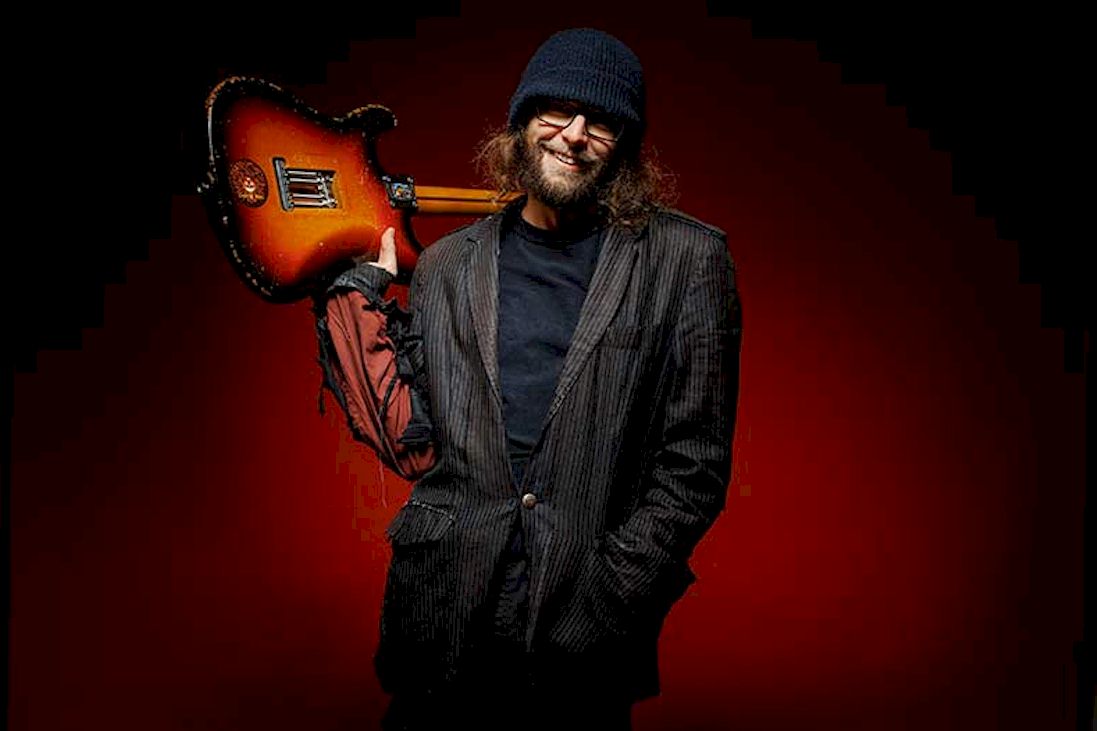RED GIANT Overcome Photo Credit © Blackham Images - man with hat and coat holding guitar on shoulder. The man has a beard and spectacles