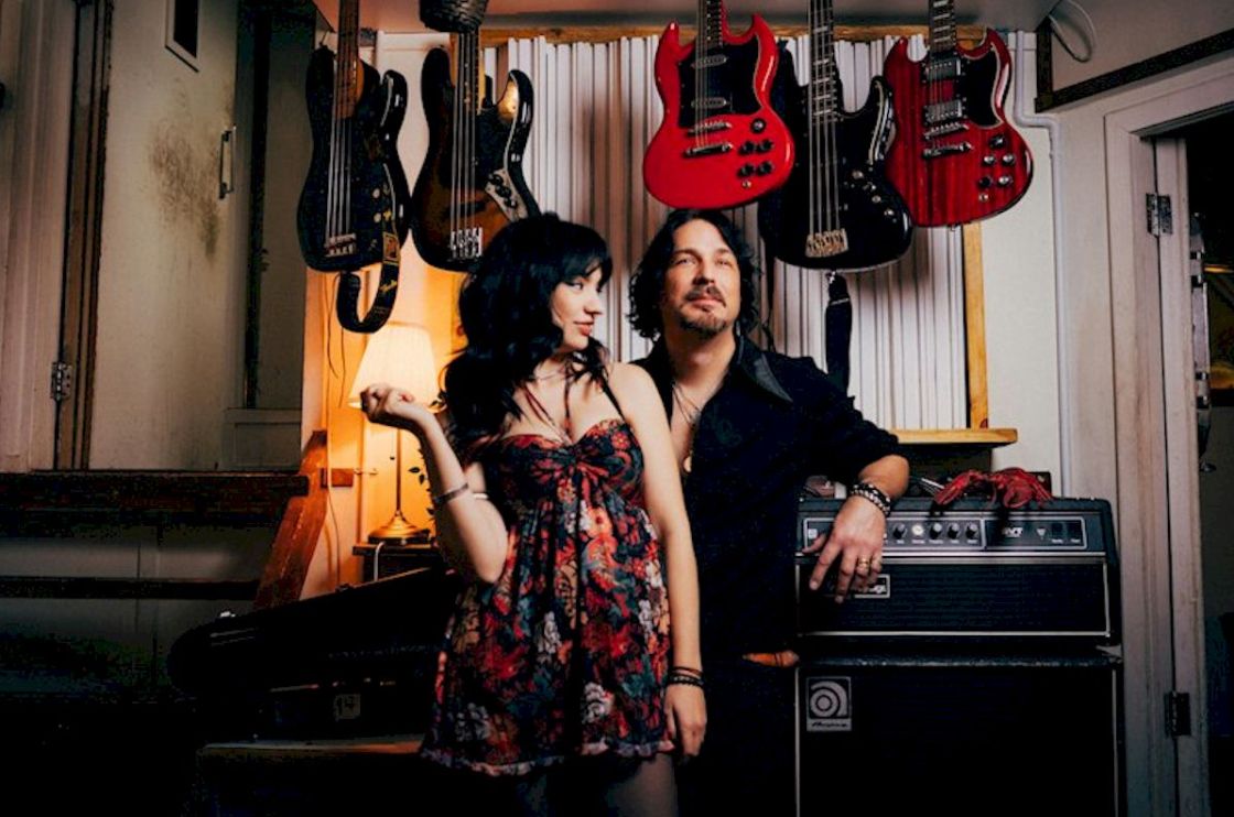 When Rivers Meet Rhythm Rust + Static - photo credit Rob Blackham - studio portrait of woman in flowery dress with man in black shirt standing by instruments and amplifiers
