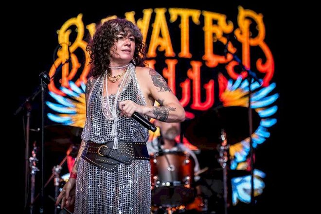 BYWATER CALL Broken Souvenirs photo credit © Denis Carpenter - female singer wearing silvery dress with a wide belt, standing on a stage