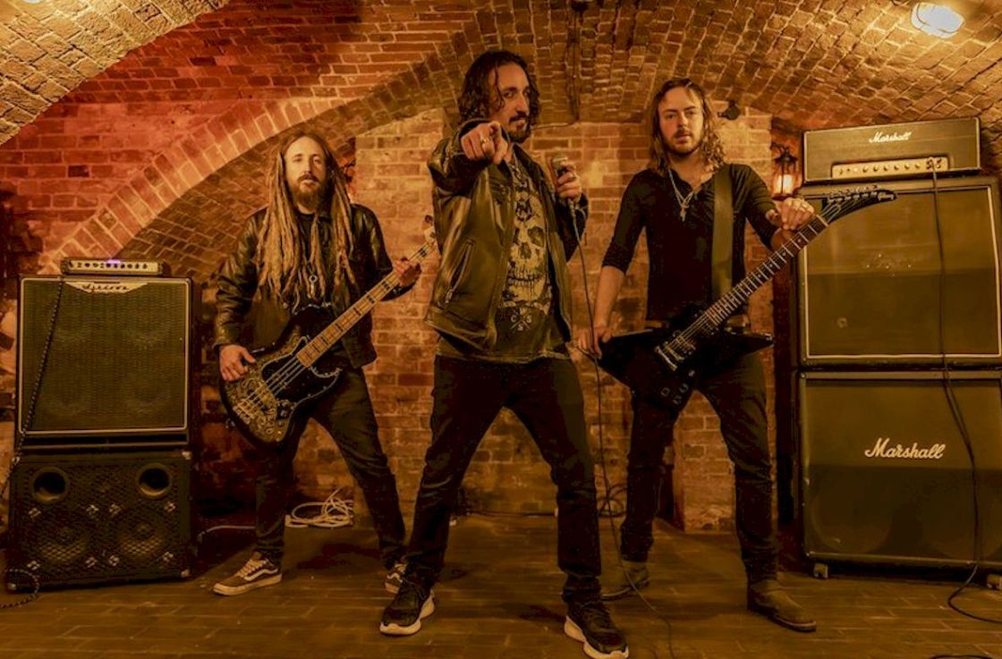 BLACK WATER REDEMPTION Album Review Lynn Burt Photography - three musicians on stage. All have long hair and black clothing. A singer, a guitarist and a bass guitarist